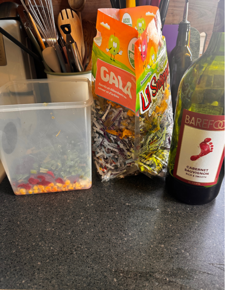 a picture of yellow, red, and green food scraps, next to a bag of shredded paper, and a bottle of red wine. Used to revive neglected compost tumbler