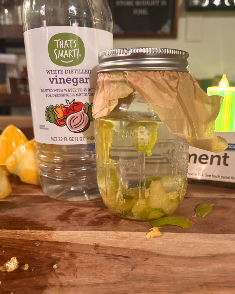 Food Waste - Mason jar with vinegar and lemon and lime peels with parchment paper sticking out from under the lid