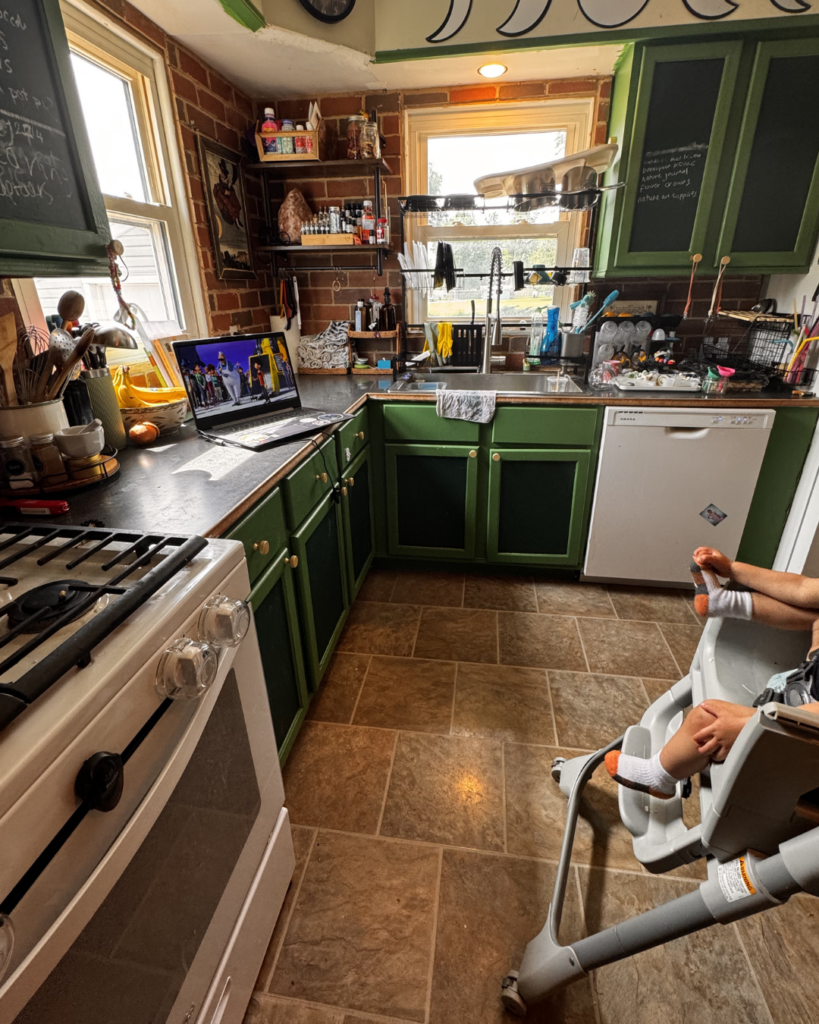 Summer rhythm - picture of previously shown kitchen now clean, with kids watching a laptop
