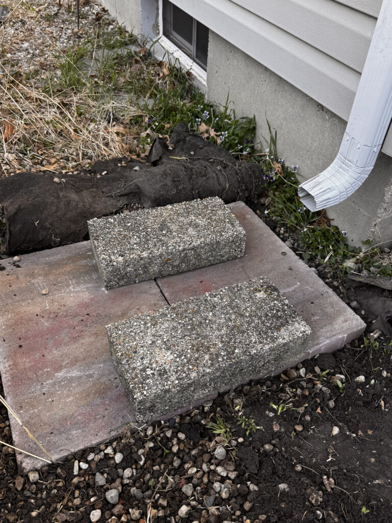 A Quick Guide to Installing a Rain Barrel - pavers on flattened ground underneath the downspout