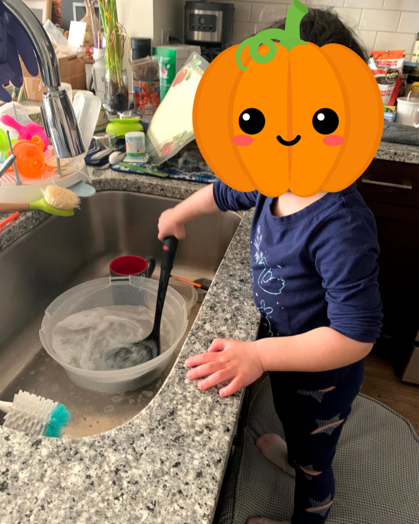 Summer rhythm - shows a child (face covered with an emoji) washing up by the sink