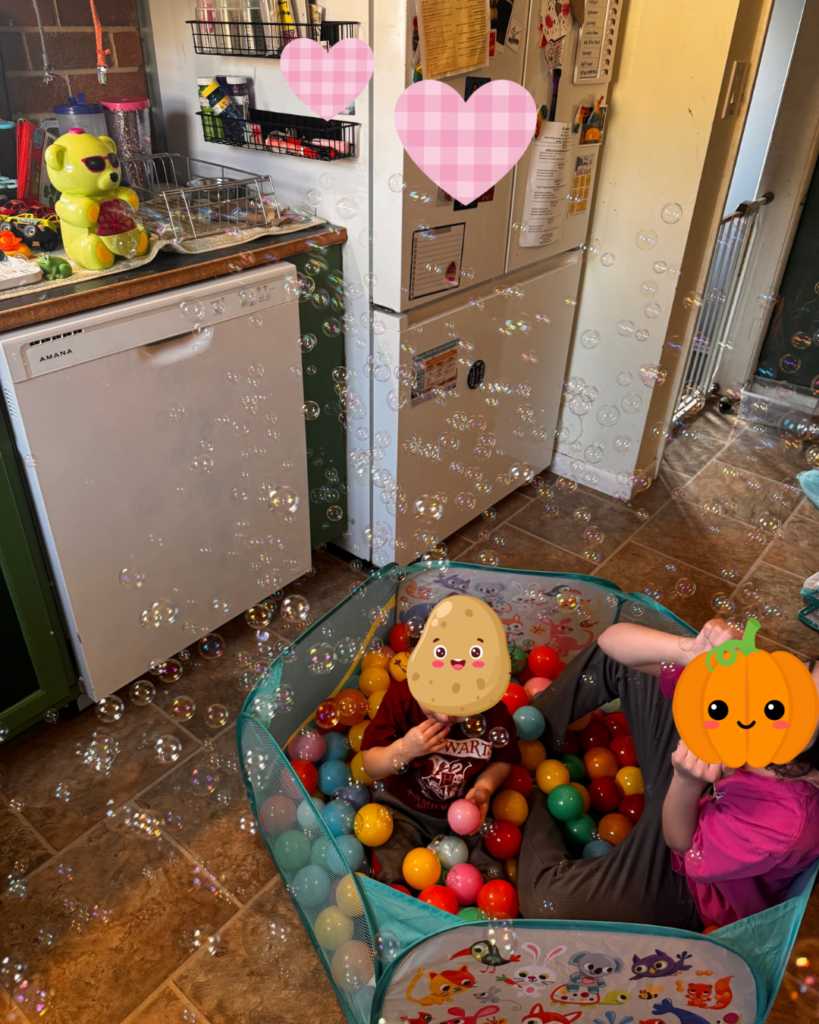 Summer rhythm - children in a ball pit in front of a dishwasher, with a bubble machine blowing. Children's faces are covered via emojis