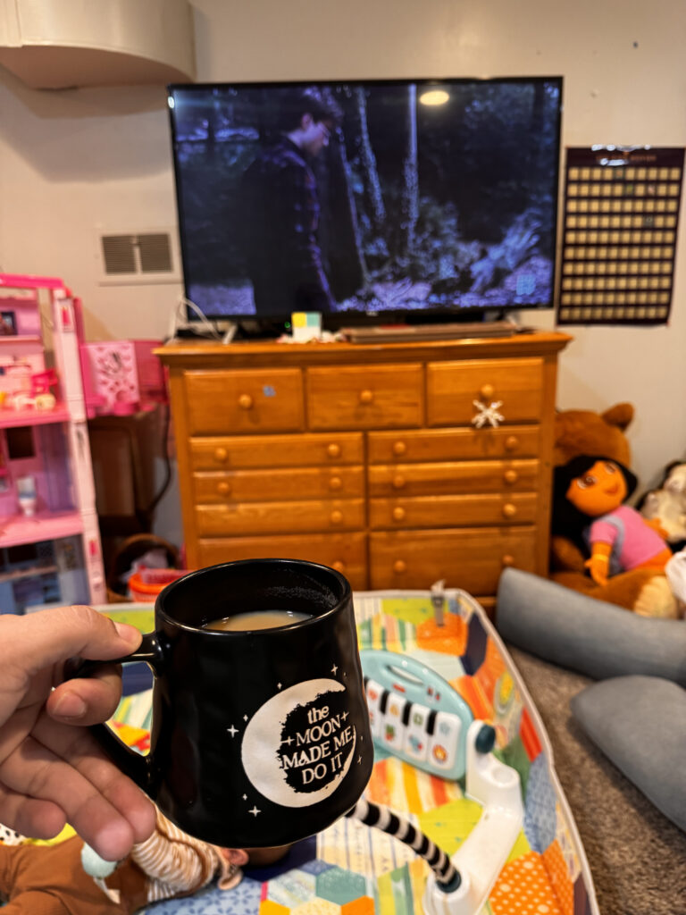 movie in background on TV, mug of tea in foreground, baby and kids toys all around