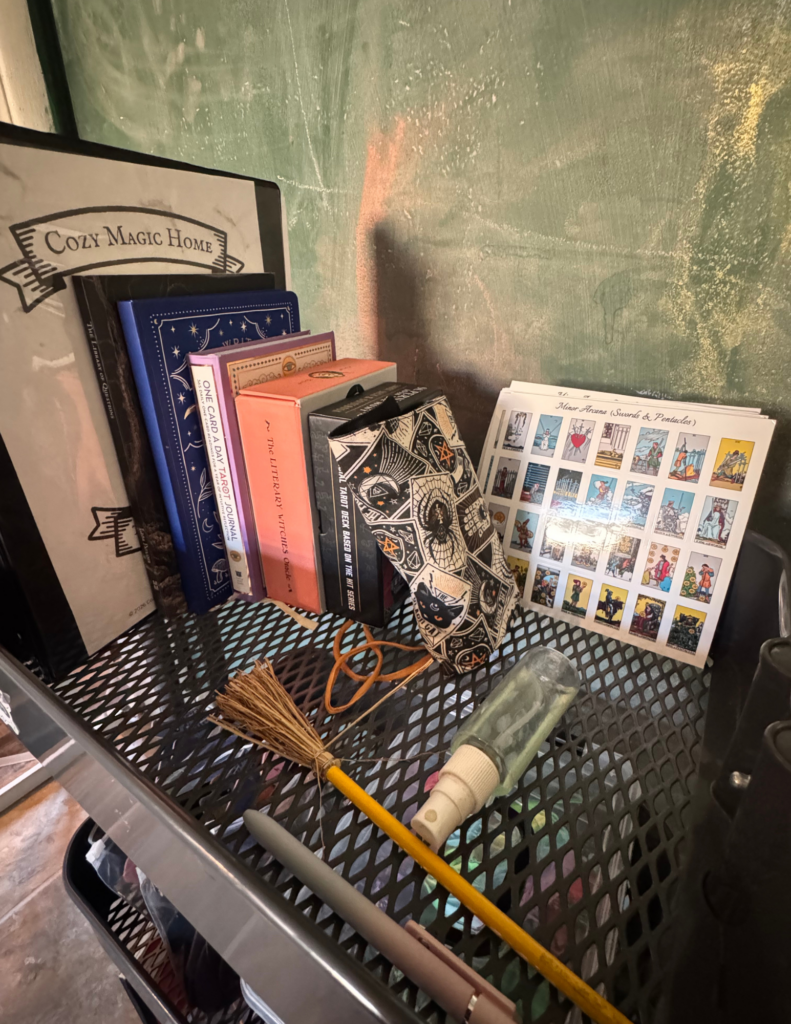 Rolling cart top held with tarot cards, stickers, a bottle of Florida Water and pen and pencil and journal